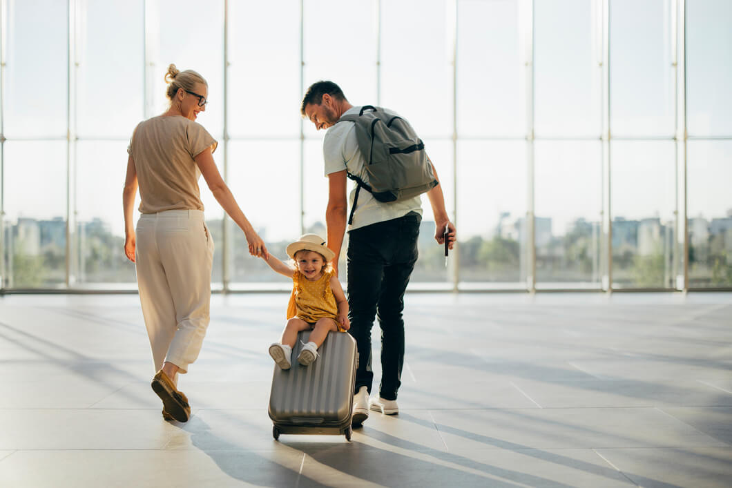 Family enjoying travel at airport terminal with child sitting on rolling luggage