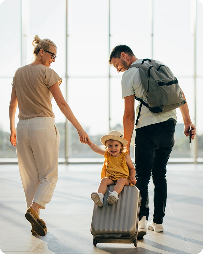 Family enjoying travel at airport terminal with child sitting on rolling luggage