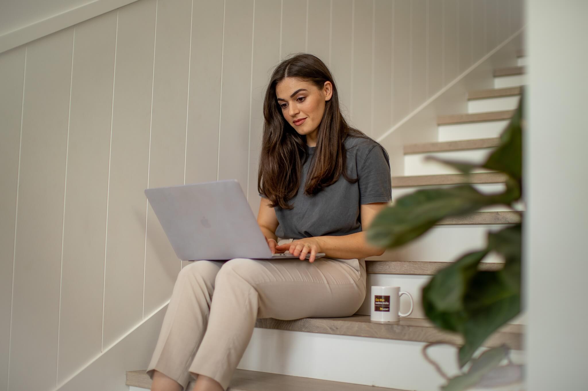Woman using laptop at home stairs planning relocation and storage with Kent Removals & Storage