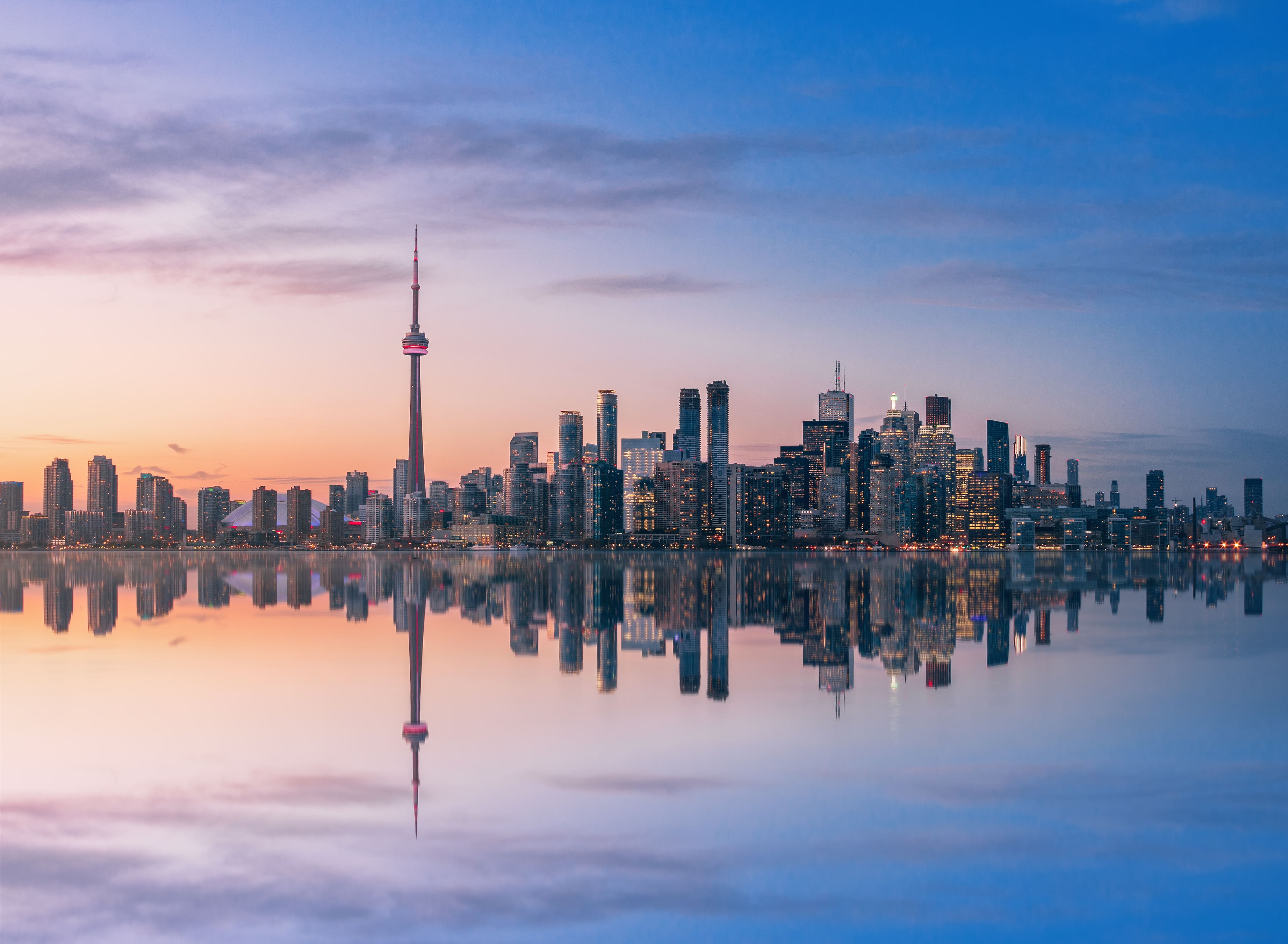 Toronto city skyline with CN Tower reflected on Lake Ontario at sunset