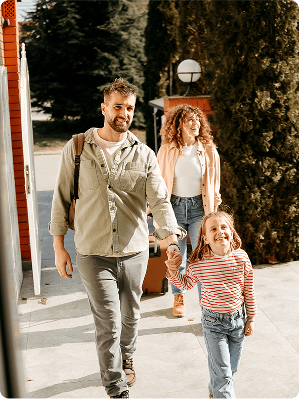 Smiling family of three walking together outdoors with luggage