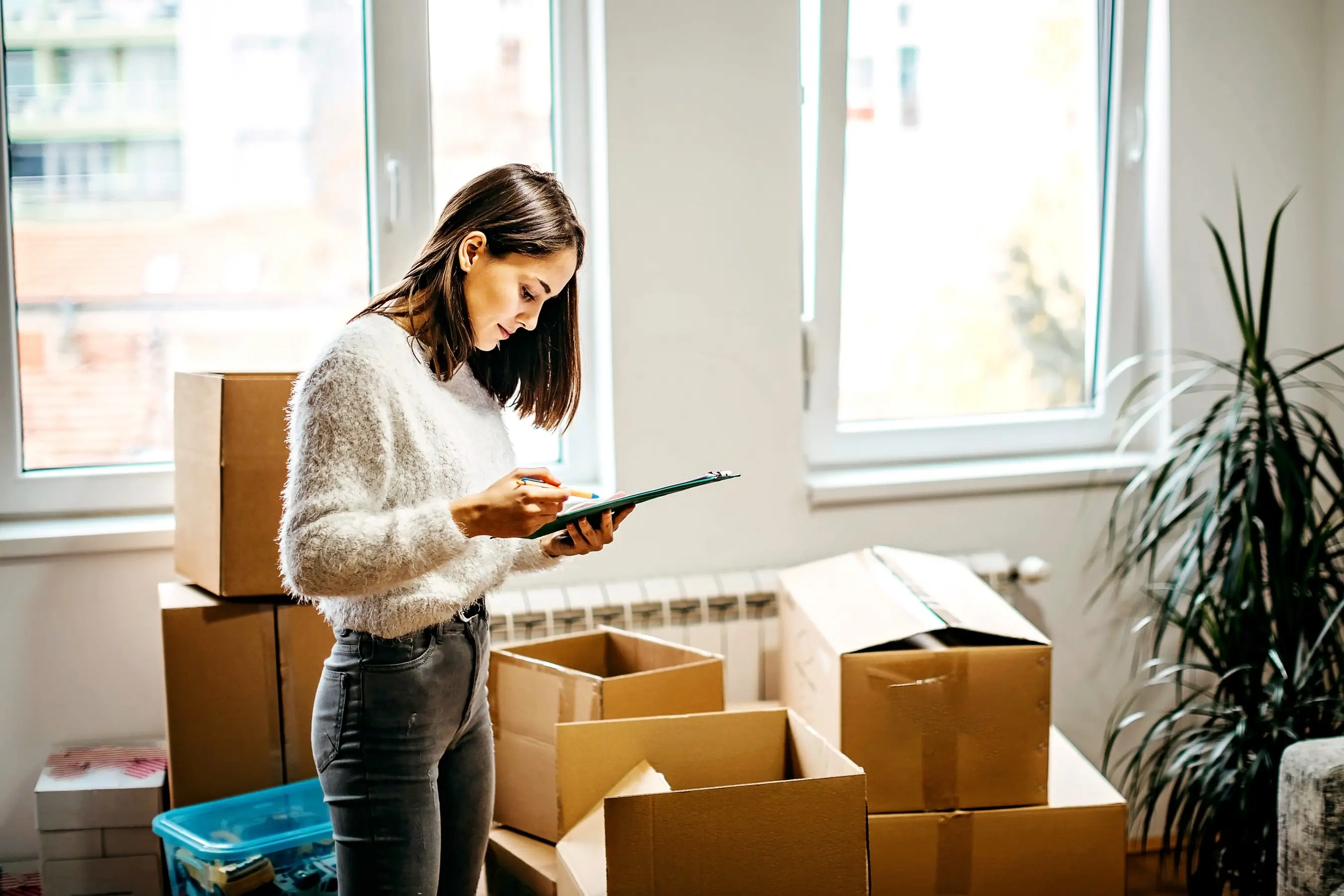 Woman checking moving checklist while packing boxes in new home
