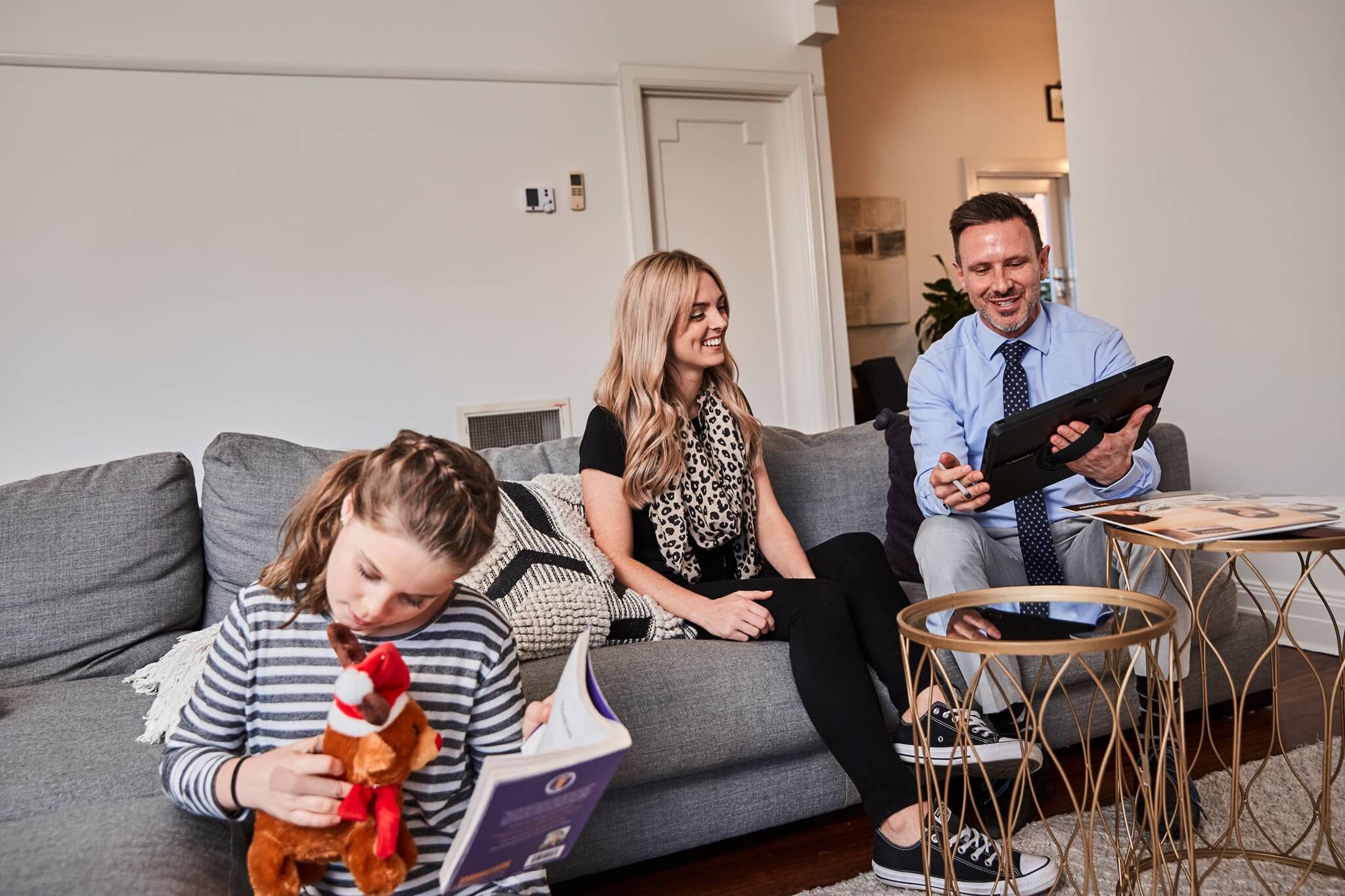 Family relaxing on sofa at home with parents looking at tablet and child reading