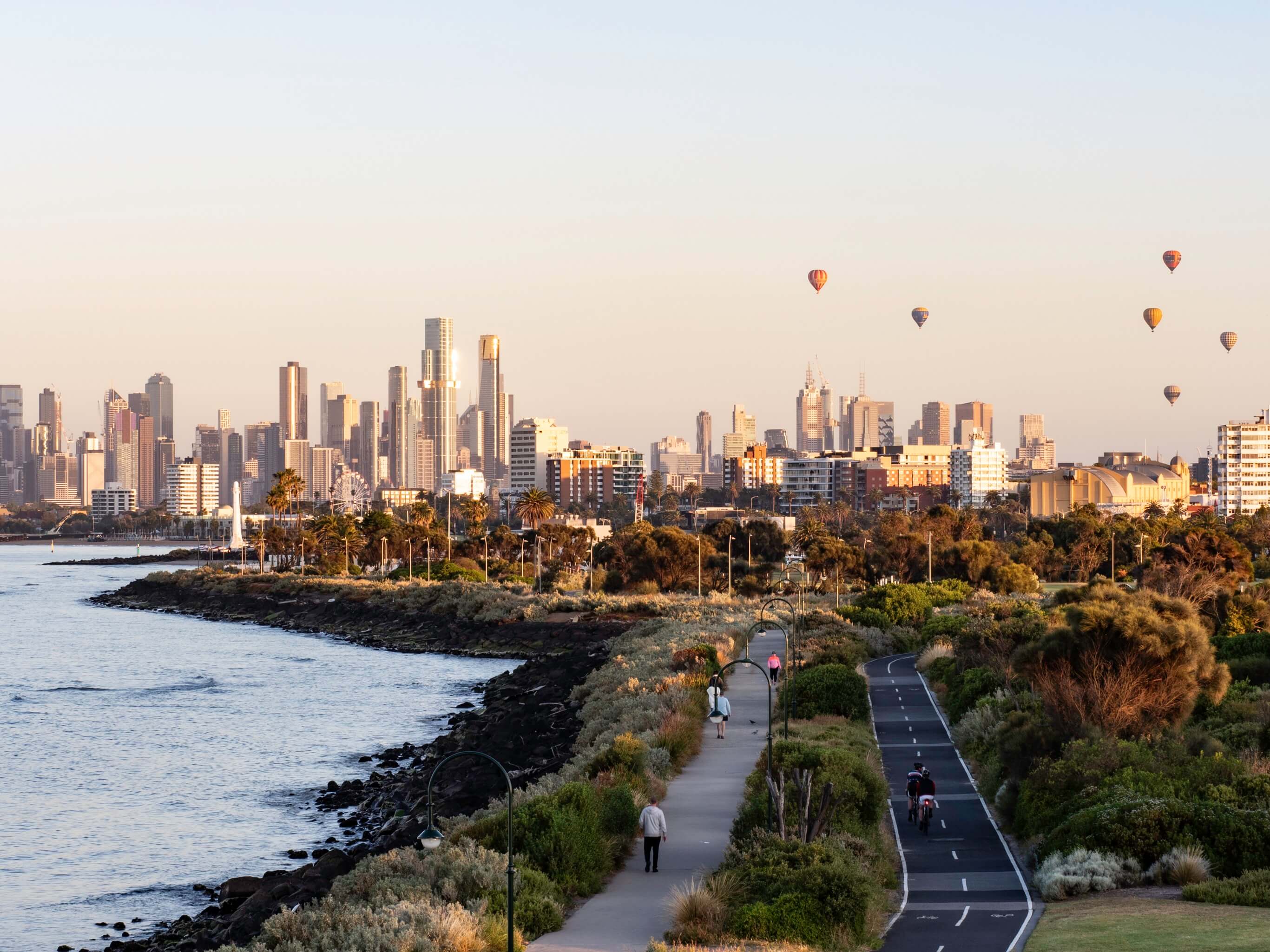 Melbourne city skyline at sunrise with hot air balloons and coastal pathway
